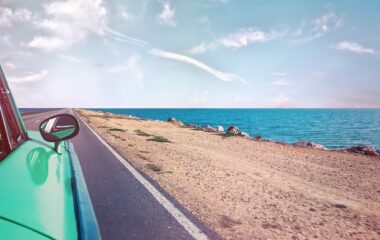 green car near seashore with blue ocean