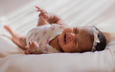 baby in a onesie lying on bed