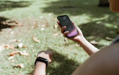 crop woman with fitness bracelet using smartphone