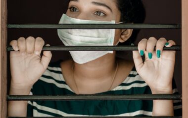 woman in green and white stripe shirt covering her face with white mask